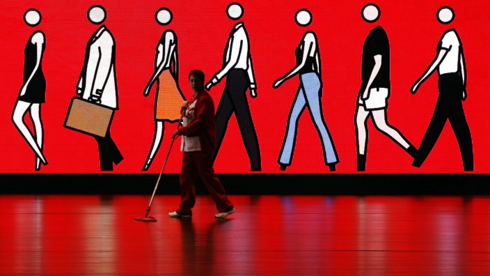 A cleaner sweeps the floor as she walks past an illuminated sign at Spain's Santander headquarters in Boadilla del Monte outside Madrid