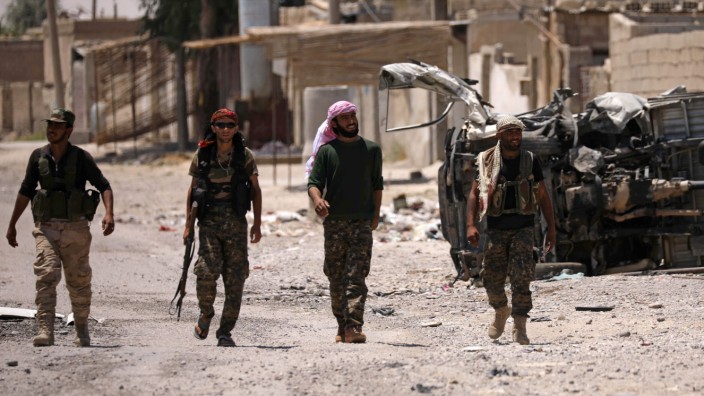 Syrian Democratic Forces (SDF) fighters walk past a damaged vehicle in Raqqa's western neighbourhood of Jazra