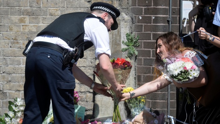 A police officer helps a woman leave flowers near the scene of an attack where a van was driven at muslims outside a mosque in Finsbury Park in North London