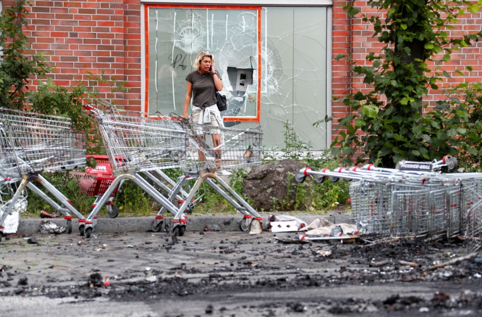 Woman uses her mobile phone in front of a supermarket, damaged during demonstrations at the G20 summit in Hamburg