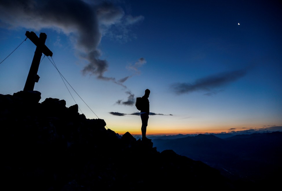 A man stands on a mountain summit as he looks over the Inntal valley in the western Austrian village of Gnadenwald