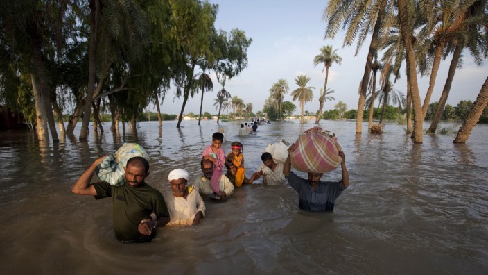 A family  wades through flood waters while evacuating Baseera, Pakistan