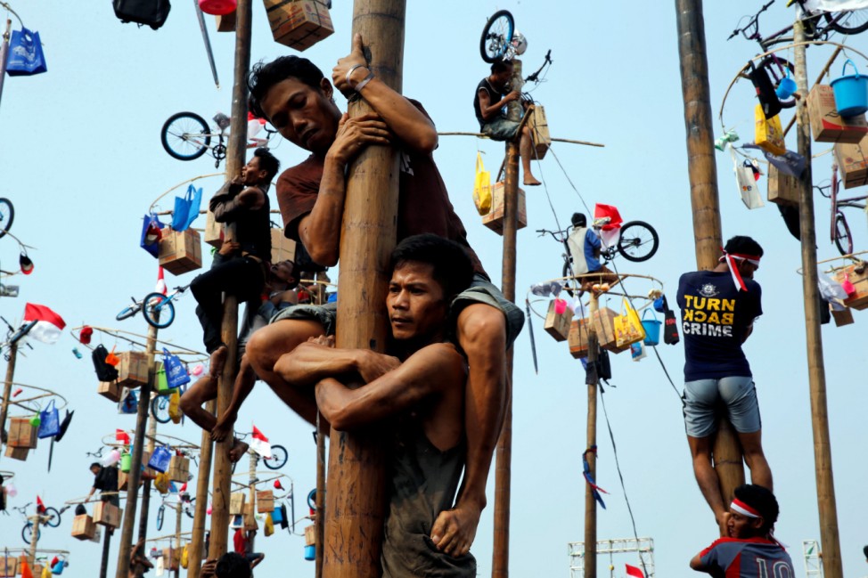 Participants react as they hold on to a greased pole during the 'Panjat Pinang' competition for the celebration of Independence Day at Ancol Dreamland Park in Jakarta