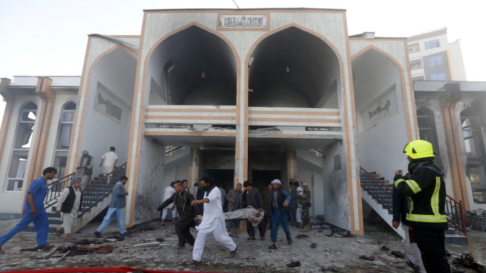 Afghan men carry a dead body from the site of a suicide attack followed by a clash between Afghan forces and insurgents after  an attack on a Shi'ite Muslim mosque in Kabul
