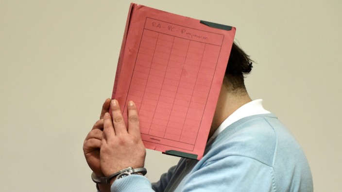 Former nurse Niels H. masks his face with a folder on his arrival in the courtroom in Oldenburg