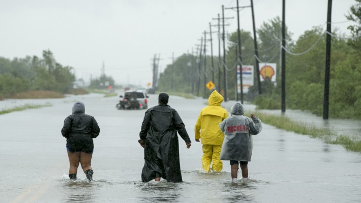 Sturm und Überschwemmungen: Leute laufen in Regencapes durch eine überflutete Straße in Beaumont im Bundesstaat Texas.