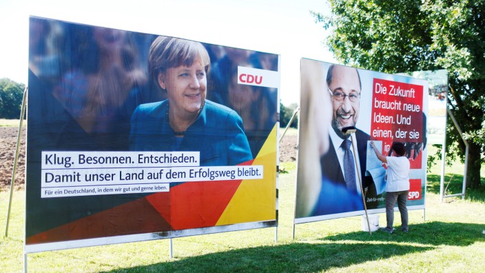 A woman glues poster of the two top candidates for the upcoming general elections, German Chancellor Merkel for the Christian Democratic Union party (CDU), and Schulz for Social Democratic Party (SPD) before an election campaign rally in Bitterfeld-Wolfen