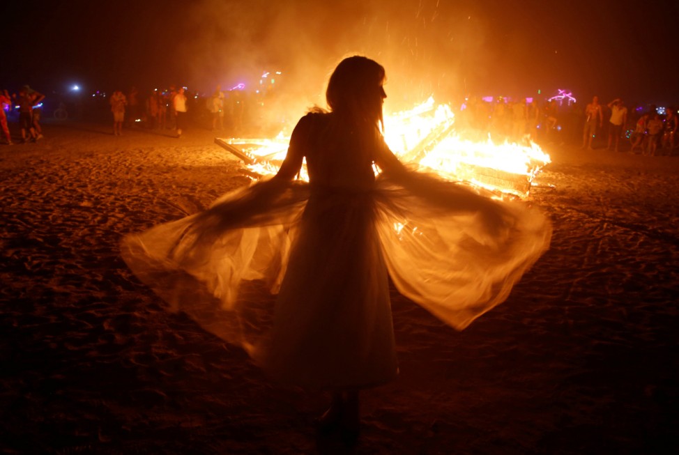 A participant dances as an art installation burns as approximately 70,000 people from all over the world gathered for the annual Burning Man arts and music festival in the Black Rock Desert of Nevada