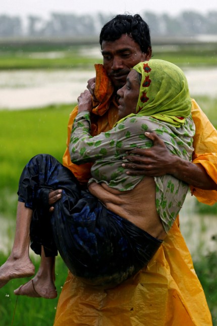 A local man carries an old Rohingya refugee woman as she is unable to walk after crossing the border, in Teknaf