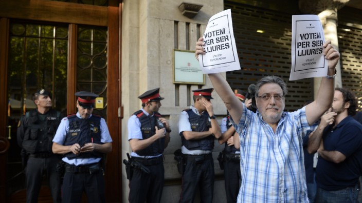 Spanien: Ein Mann vor dem katalanischen Regierungssitz hält Wahlplakate für das Referendum hoch, während spanische Polizisten der Guardia Civil (li.) das Gebäude durchsuchen.