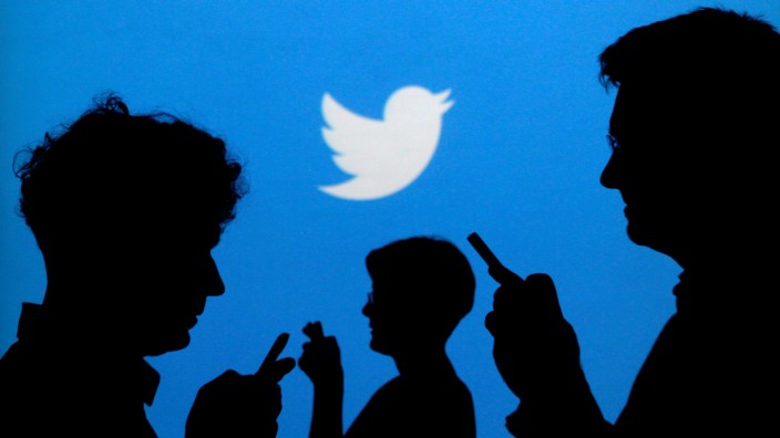 FILE PHOTO: People holding mobile phones are silhouetted against a backdrop projected with the Twitter logo