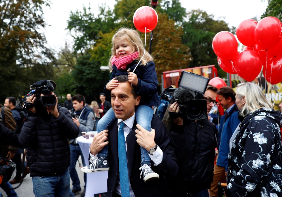 Austrian Chancellor Kern holds a child during the presentation of his party's election campaign posters in Vienna