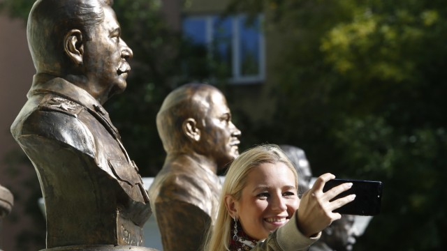 A woman takes a selfie while standing in front of the busts of Soviet leader Stalin and Soviet state founder Lenin at the Alley Of Rulers in Moscow