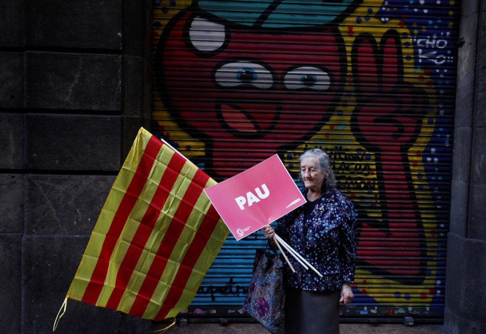 A woman carrying a Catalan flag and a sign reading 'Peace' walks to join a pro-union demonstration organised by the Catalan Civil Society organisation in Barcelona