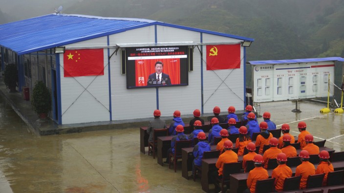 China: Vorsitzender von allem: Straßenarbeiter lauschen einer Rede von Xi Jinping, die über einen Bildschirm übertragen wird.
