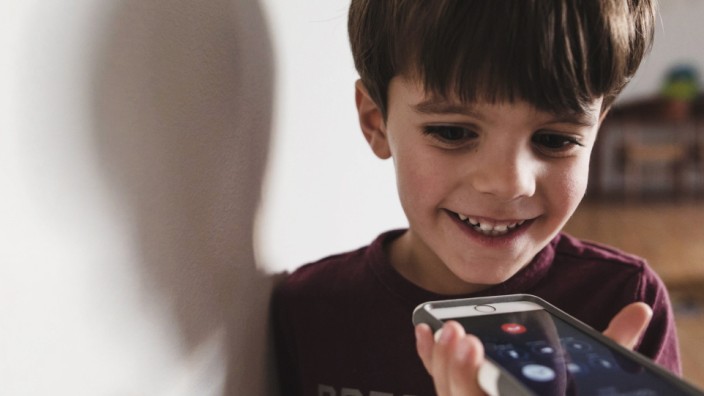 Smiling boy with brown hair standing indoors holding smartphone Smiling boy with brown hair standi