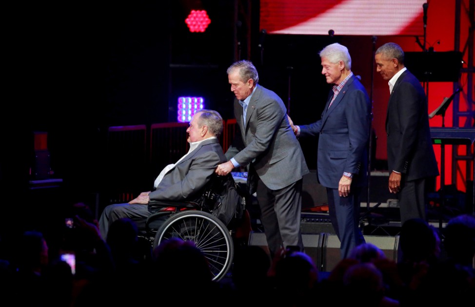 Former U.S. President George H.W. Bush is helped off the stage by George W. Bush as Bill Clinton and Barack Obama follow close behind during a concert at Texas A&M University