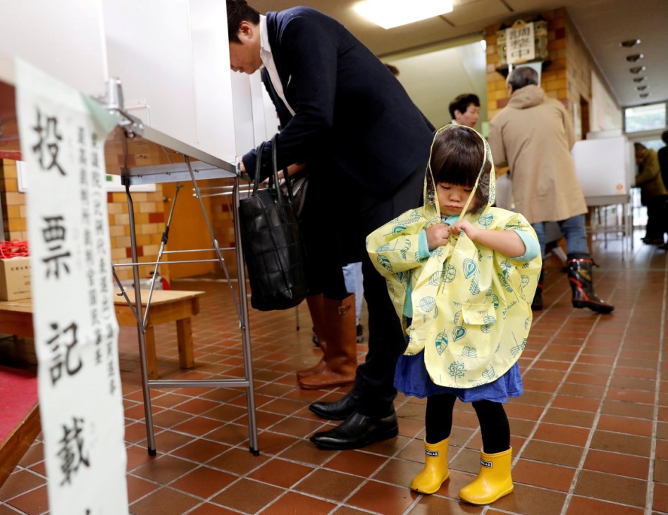 A girl stands next to her father filling out his ballot for a national election at a polling station in Tokyo