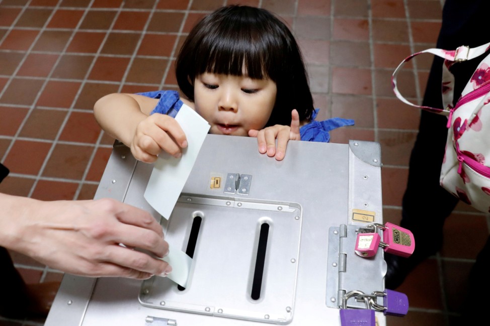 A girl casts her father's ballot for a national election at a polling station in Tokyo