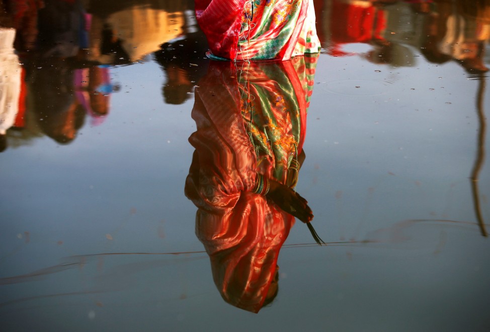 The reflection of a woman is seen in the waters of the Sabarmati River as she worships the Sun god during the religious festival of Chhath Puja in Ahmedabad