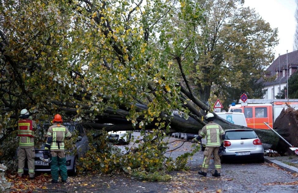 Firefighters are pictured next to a car damaged by a tree during stormy weather caused by a storm called 'Herwart' in Berlin