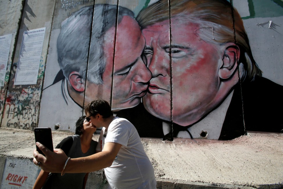 Tourists kiss each other as they stand in front of a mural depicting U.S. President Donald Trump and Israel's Prime Minister Benjamin Netanyahu kissing each other in the West Bank city of Bethlehem