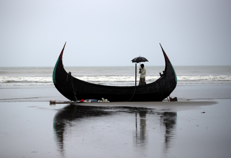 A man holds an umbrella as he stands on a boat, which capsized with a group of Rohingya refugees at Bailakhali, near Cox's Bazar