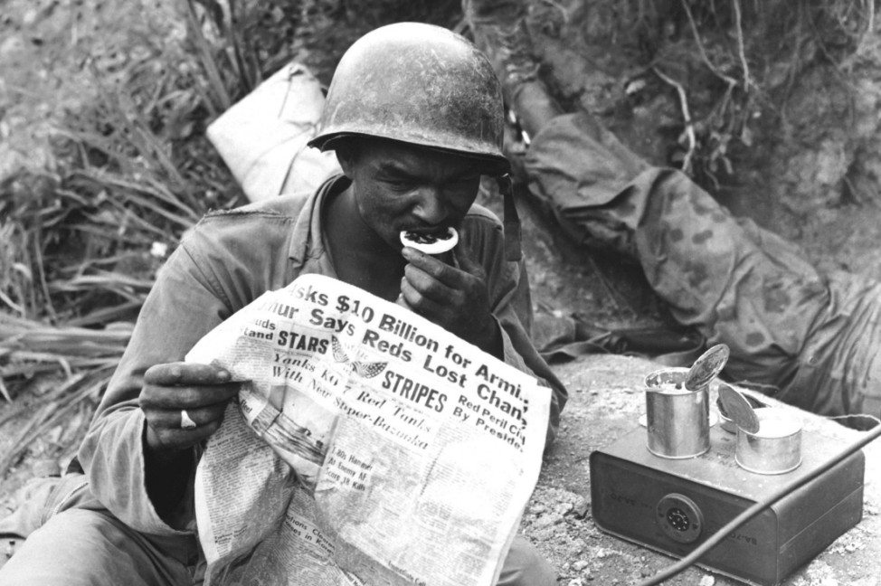 August 9 1950 U S soldier reads the latest news while enjoying chow during lull in battle agains