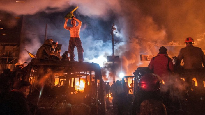 Jan 25 2014 Kiev Ukraine A protester on a burned bus holds a chainsaw as confrontations betwe