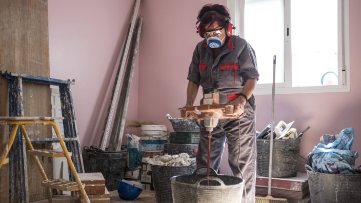 Senior woman using stirrer for mixing paint at construction site model released Symbolfoto property