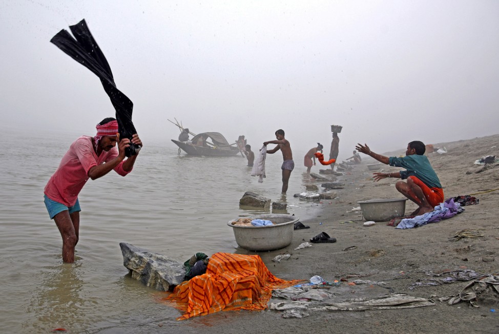 People wash clothes on the banks of the river Brahmaputra on a foggy winter morning in Guwahati