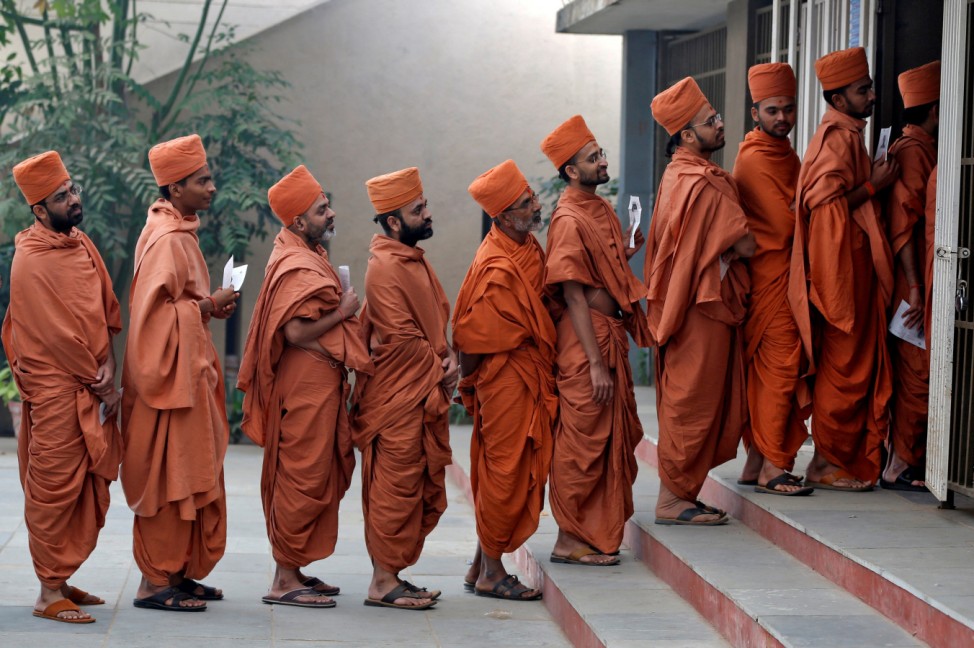 Hindu saints stand in a queue to casts their votes at a polling station during the last phase of Gujarat state assembly election on the outskirts of Ahmedabad
