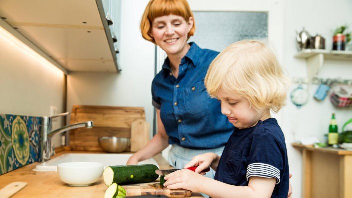 Littel boy chopping vegetables in the kitchen while his mother watching him model released Symbolfot