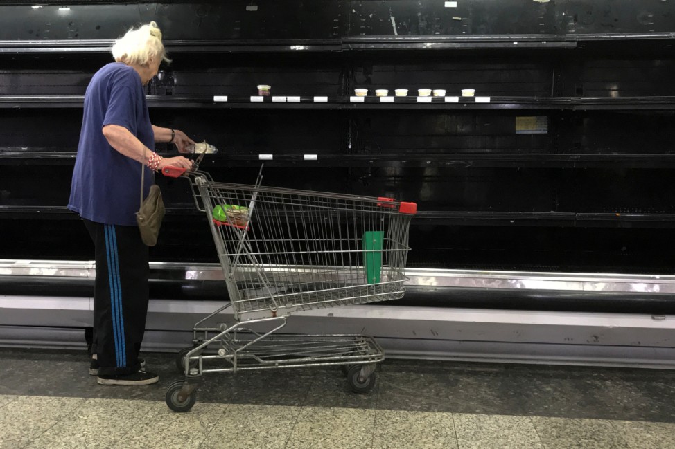 A woman selects goat cheese from partially empty refrigerators at a supermarket in Caracas
