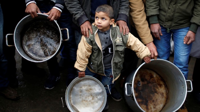 A Palestinian boy holds cooking pots during a protest against aid cuts, outside United Nations' offices in Gaza City