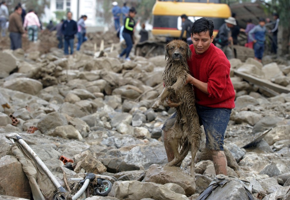 A man carries a dog from mud and stones after a river flooded Tiquipaya due to heavy rains, in Tiquipaya