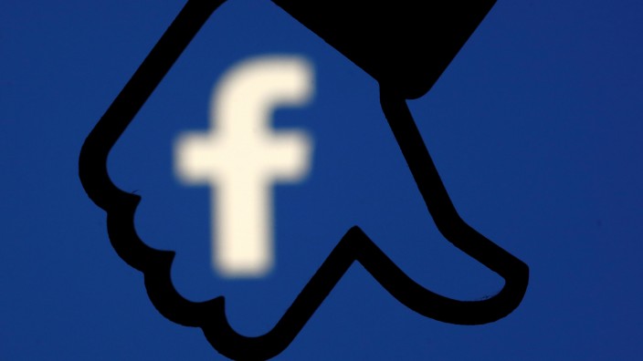 A 3D-printed Facebook dislike button is seen in front the Facebook logo, in this illustration