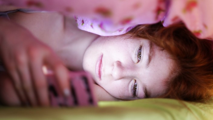 Portrait of girl lying under blanket in bed looking at her smartphone model released Symbolfoto PUBL