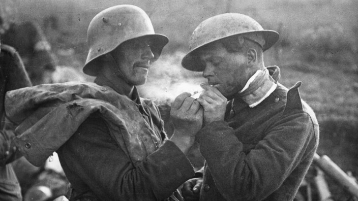 Ein deutscher Gefangener gibt einem britischen Verwundeten (re.) Feuer. Die Aufnahme entstand an der Westfront im Jahre 1918.