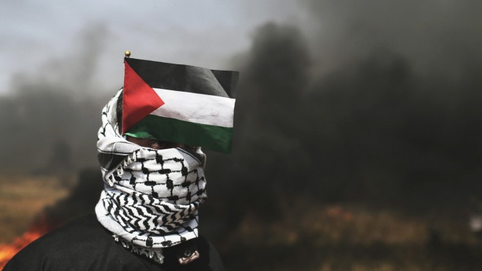 Demonstrator with a Palestinian flag looks on during clashes with Israeli troops at the Israel-Gaza border at a protest demanding the right to return to their homeland, in the southern Gaza Strip