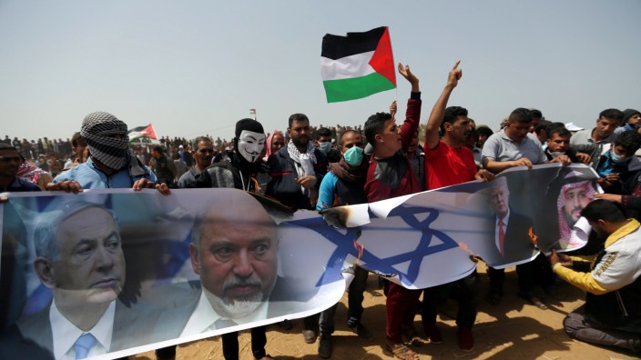 Palestinian demonstrators burn a banner showing a representation of an Israeli flag and pictures of Netanyahu, Lieberman, Trump, and bin Salman during a protest at the Israel-Gaza border, in the southern Gaza Strip