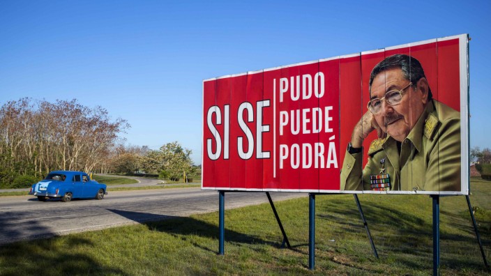 Kuba: Ein Auto fährt auf einer Straße bei Havanna an einem Plakat mit dem Bild Raúl Castros vorbei.