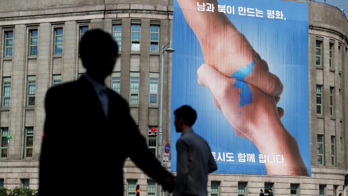 People walk past a large banner adorning the exterior of City Hall ahead of the upcoming summit between North and South Korea in Seoul