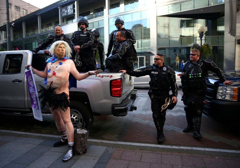 A man in a Trump outfit poses in front of a group of Seattle Police officers at Westlake Park on May Day in Seattle