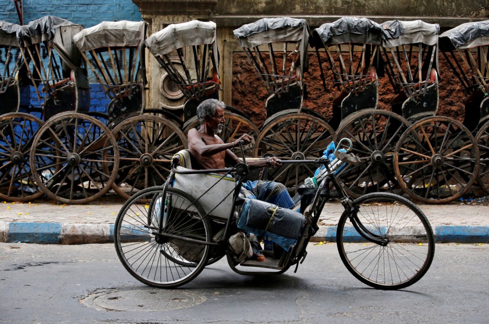 A disabled man paddles his tricycle as he moves past a row of parked hand-pulled rickshaws in Kolkata