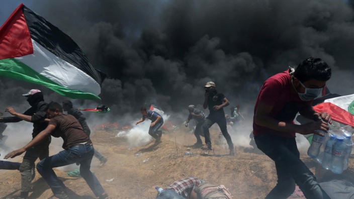 Palestinian demonstrators run for cover from Israeli fire and tear gas during a protest against U.S. embassy move to Jerusalem and ahead of the 70th anniversary of Nakba, at the Israel-Gaza border in the southern Gaza Strip