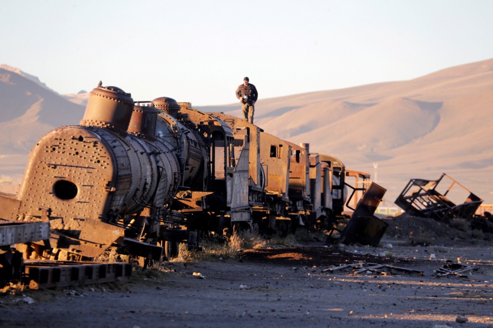 A man stands on an old train of Bolivian Railways Company from 1870-1900 at the train cemetery in Uyuni