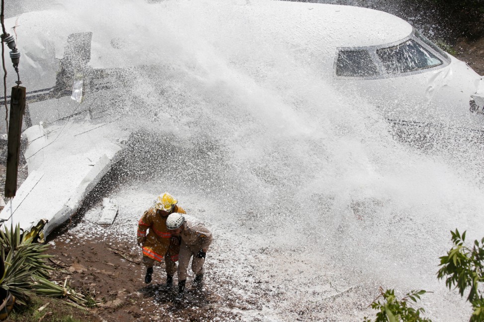 Firefighters take cover from firefighting foam applied onto the wreckage of a Gulfstream G200 aircraft that skidded off the runway during landing at Toncontin International Airport in Tegucigalpa