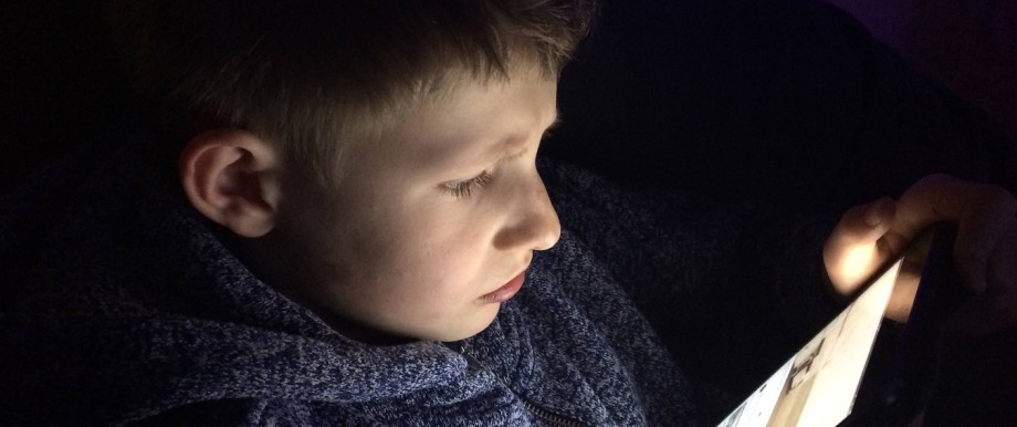 Kind Junge Schulkind schaut gebannt auf ein Tablet und liest schaut Filme an Smartphone Handy Comput