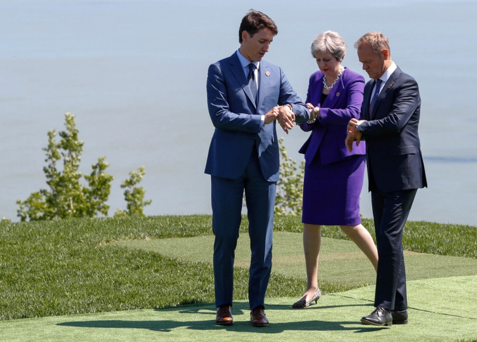 Leaders look at their watches as they pose for family photo at the G7 Summit in La Malbaie, Quebec